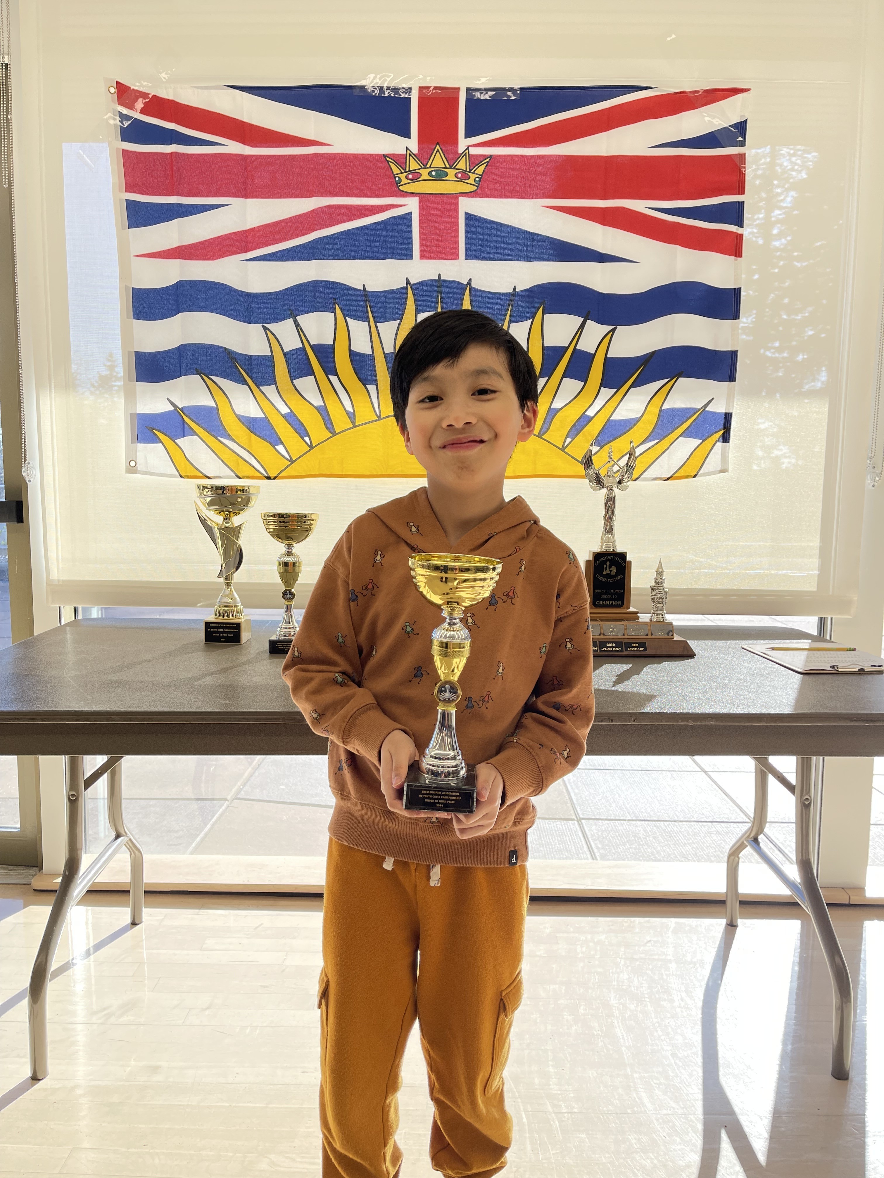 Lucas Yao holding a chess trophy near the British Columbia flag