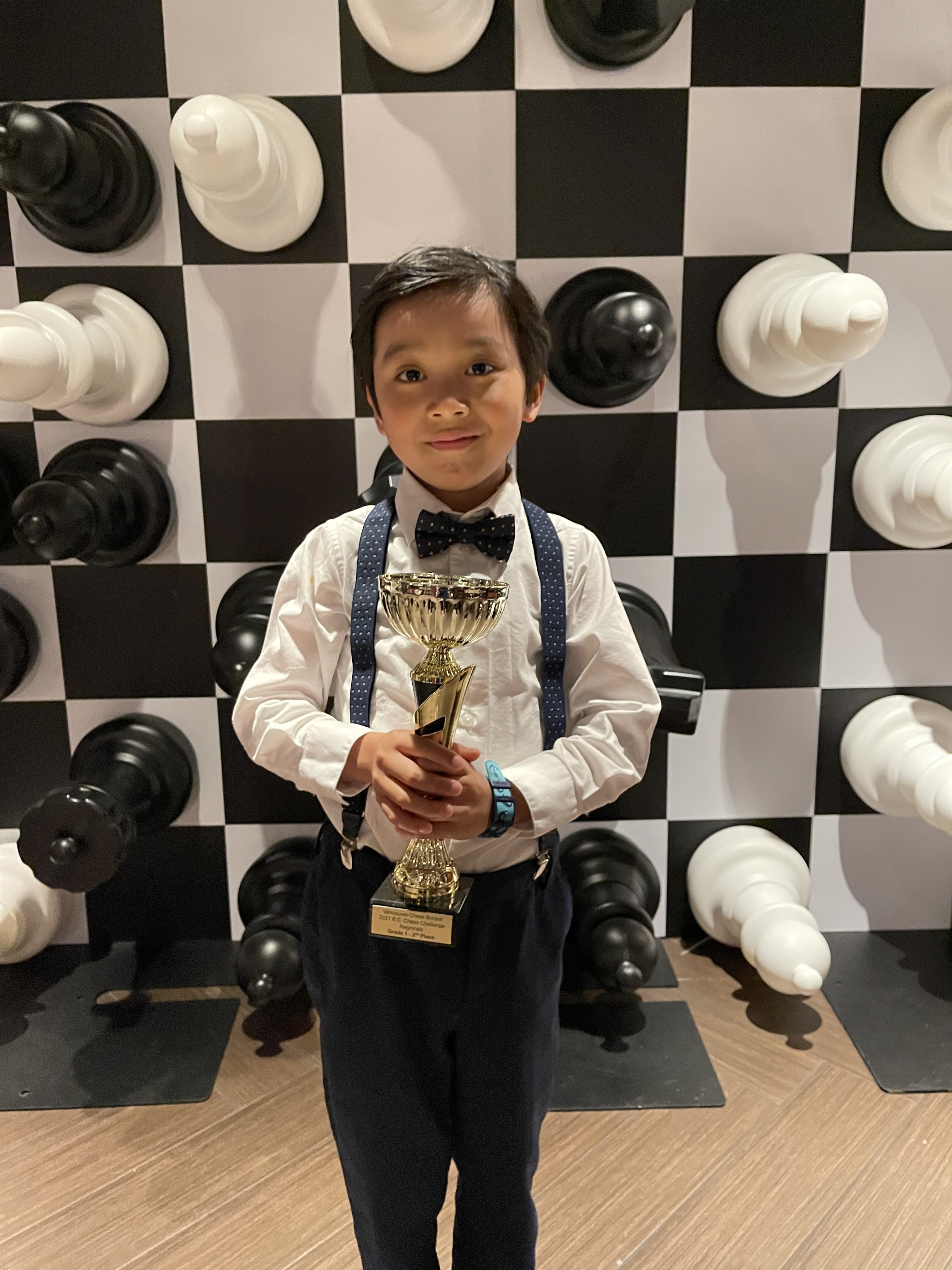 Lucas Yao holding a trophy in front of a large chessboard